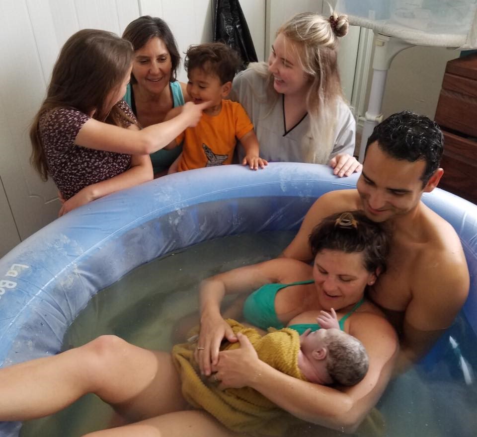 Photo of woman in birth pool with baby and family